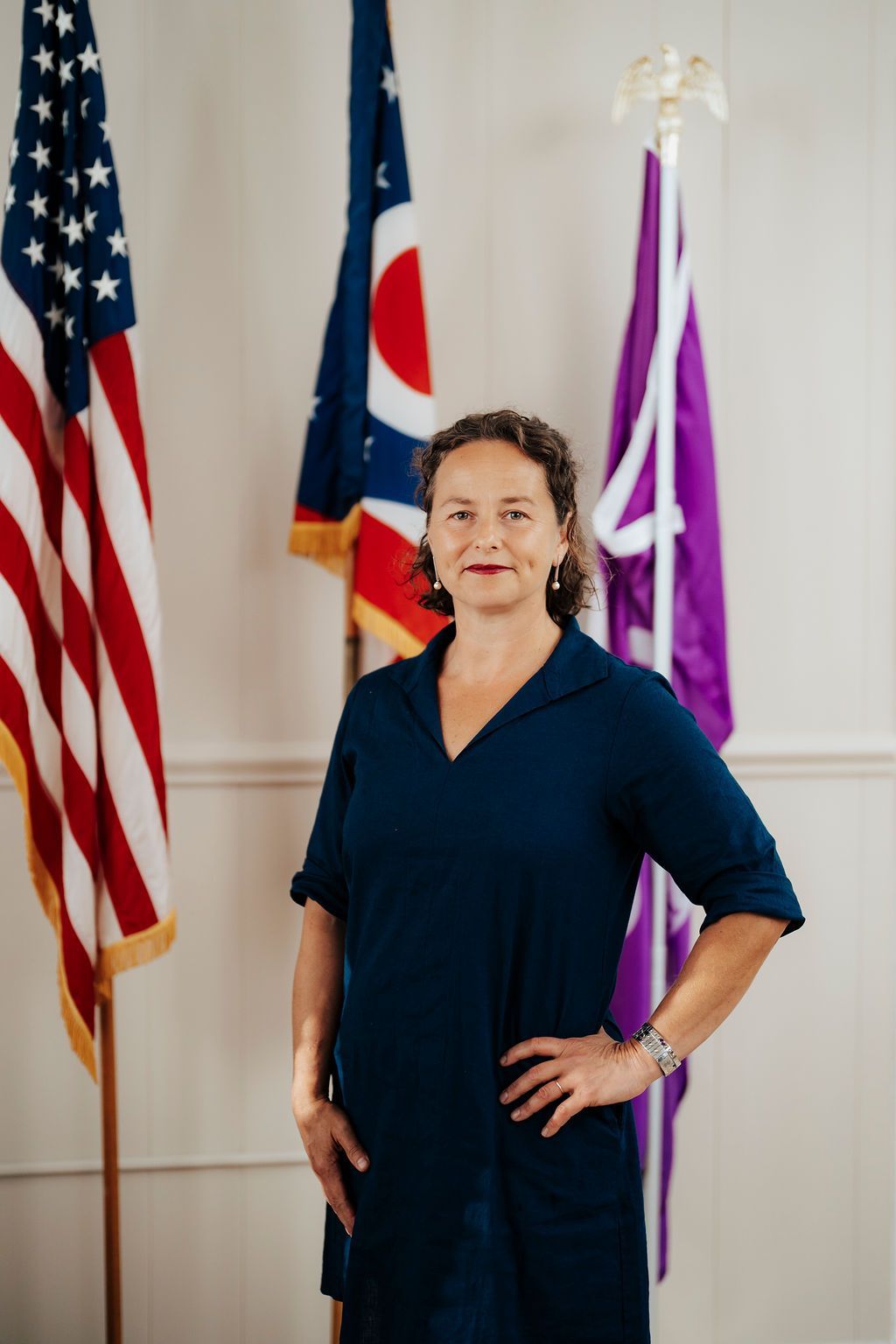 A woman in a blue dress is standing in front of three flags.