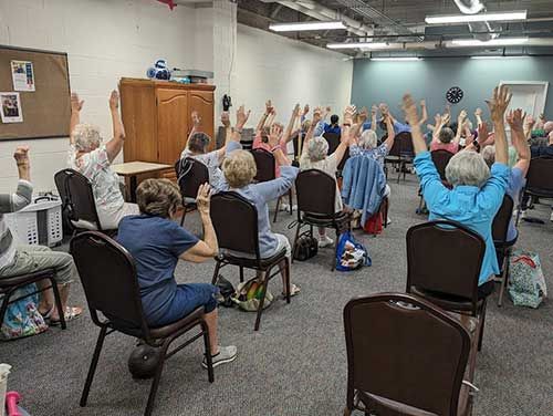 A group of people are sitting in chairs with their hands in the air.
