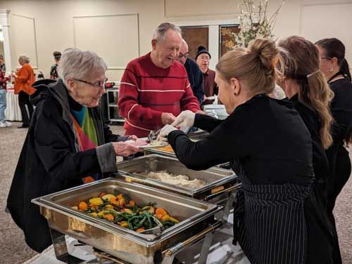 A group of people are standing around a buffet table.