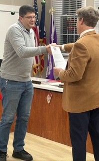 A man in a suit and tie is standing in front of three flags.