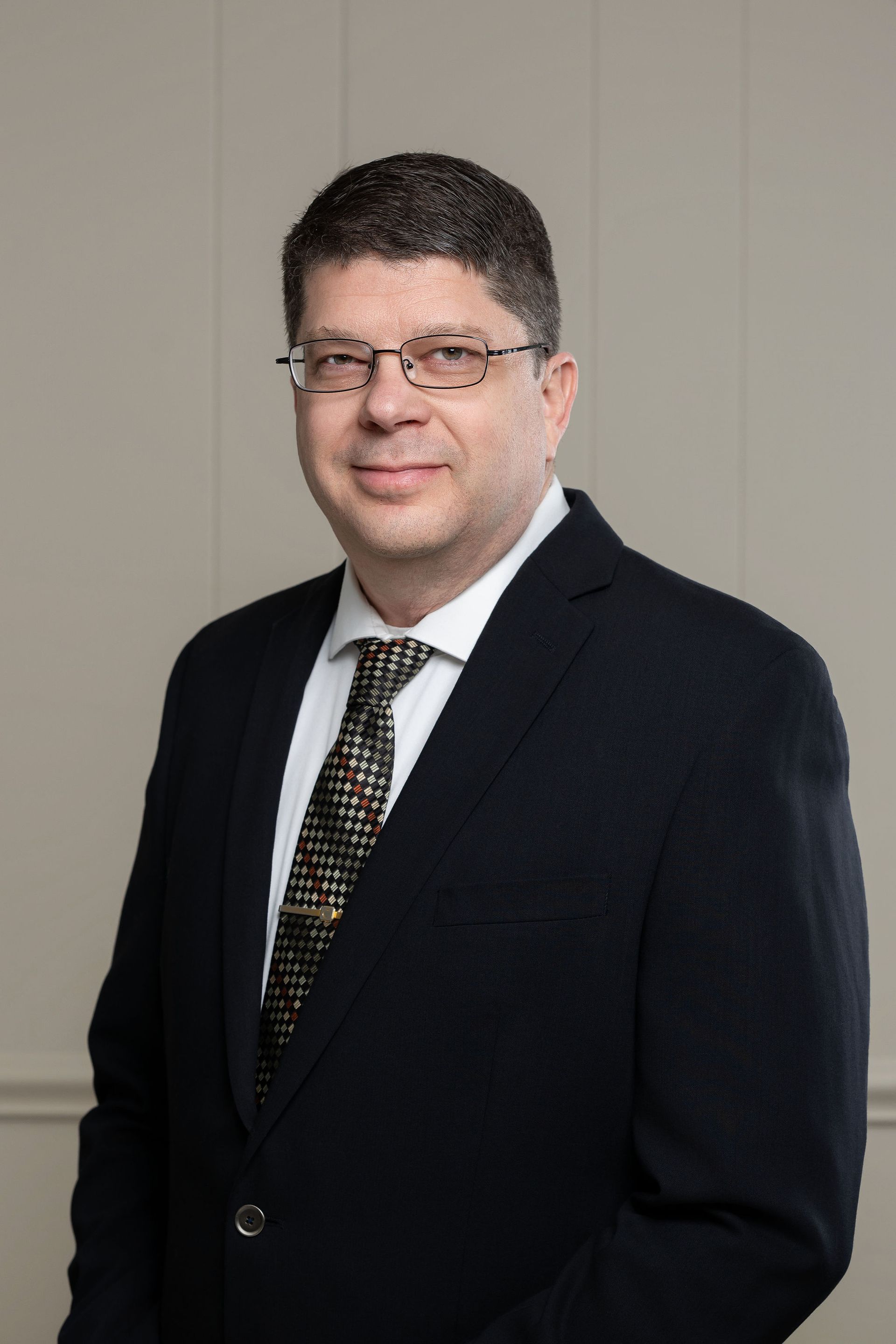 A man in a suit and tie is standing in front of three flags.
