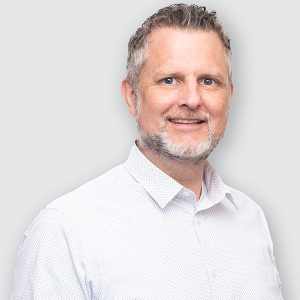 A man with a beard is wearing a white shirt and smiling.