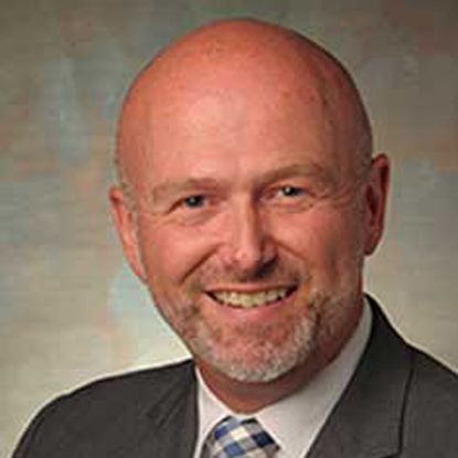 A man with a beard is wearing a suit and tie and smiling.