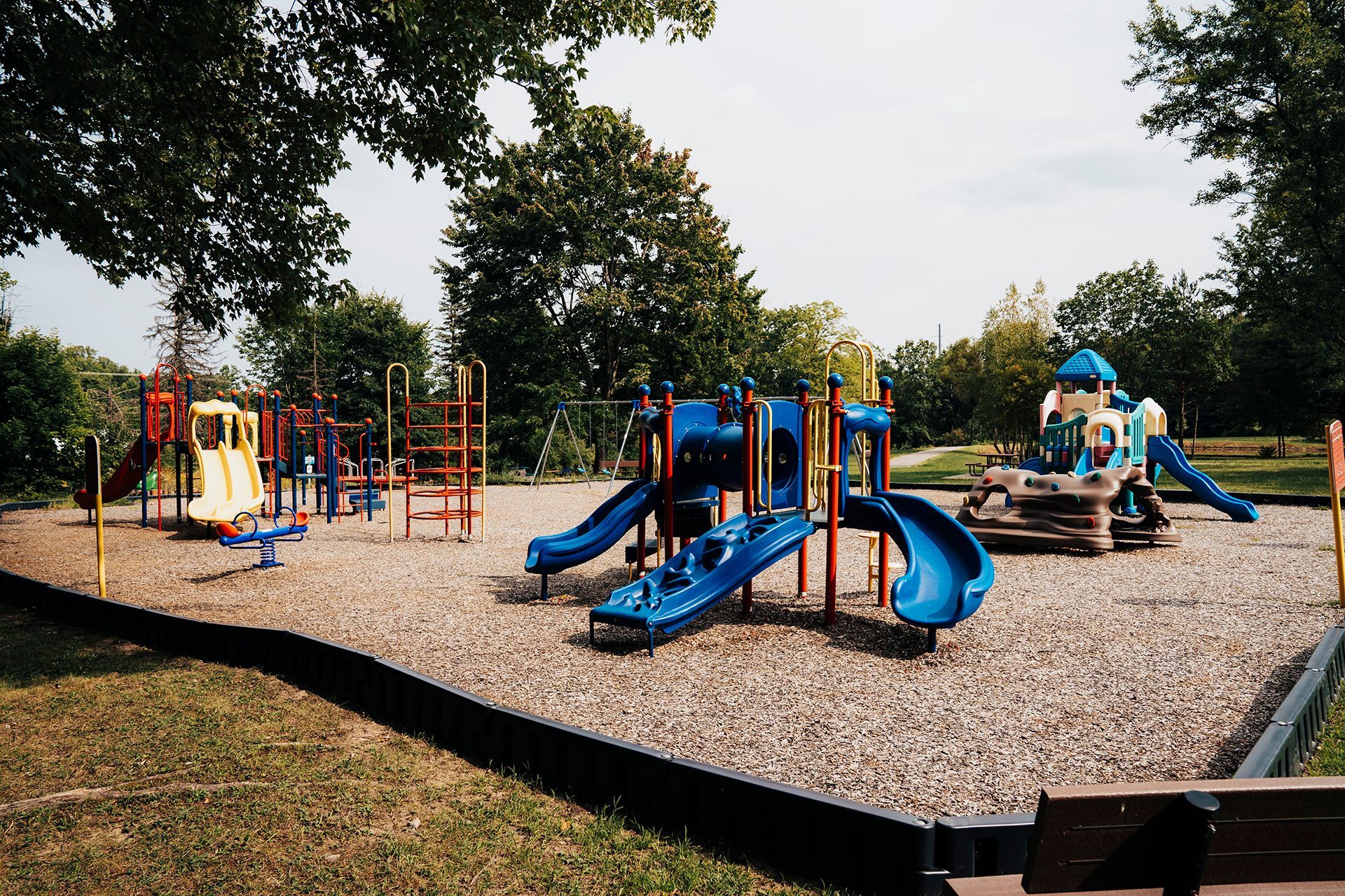 A playground with a bench in the foreground and trees in the background