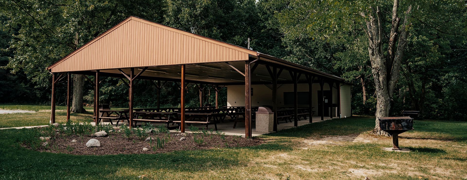 A pavilion with tables and chairs in a park surrounded by trees.