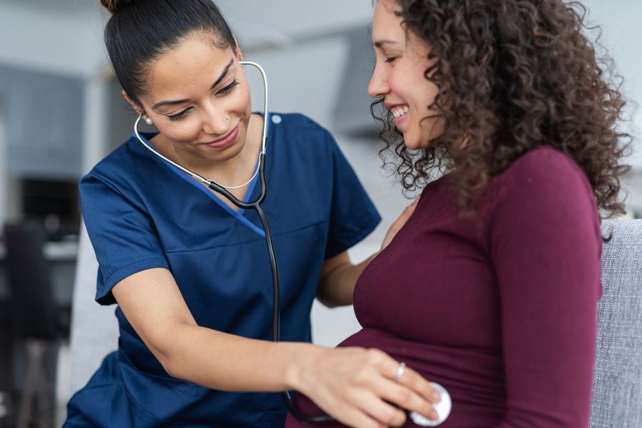 A nurse is listening to a pregnant woman 's belly with a stethoscope.