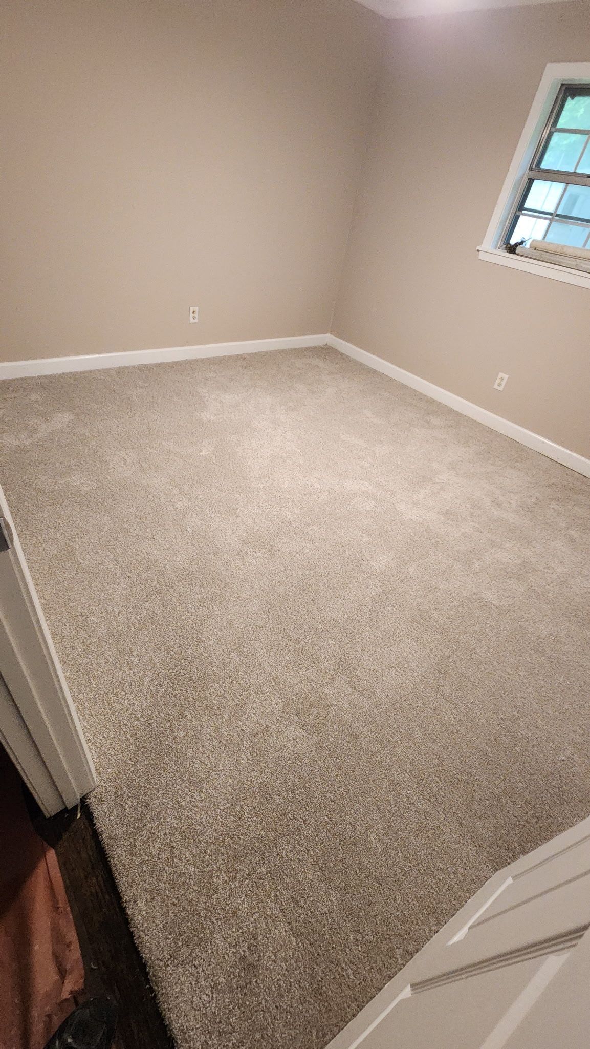Empty room with beige walls and light brown carpet. Small window on the right.