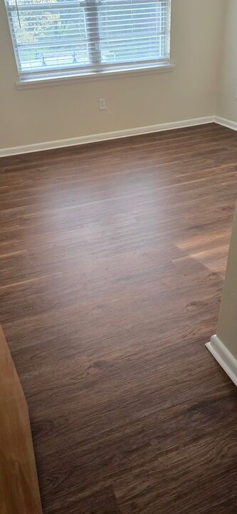 Room with dark wood-look flooring and a window with blinds. Beige walls and white trim.