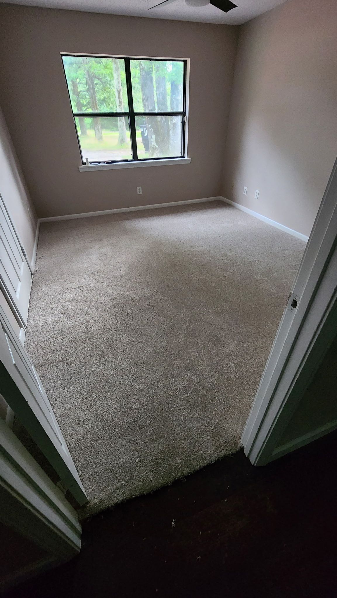 Empty bedroom with beige carpet, a window, and neutral walls, viewed from doorway.