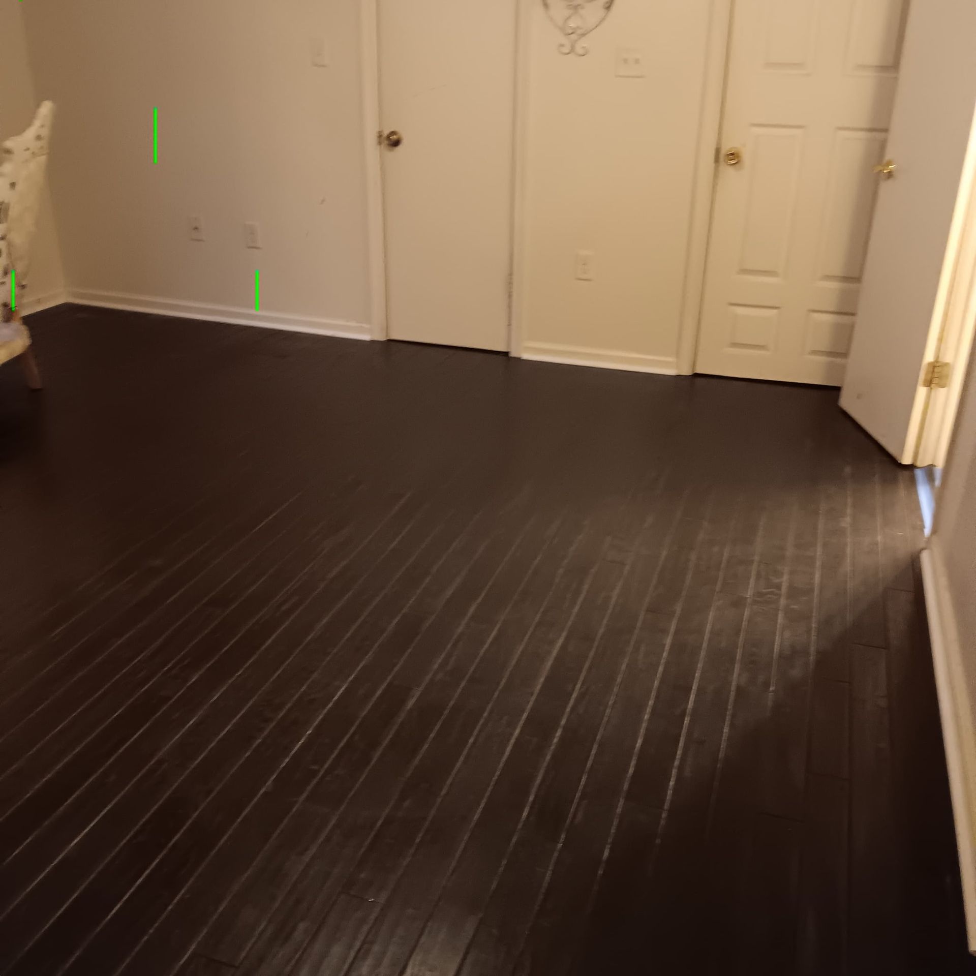 Dark hardwood floor in a room with white doors and walls; a partial view of a chair on the left.