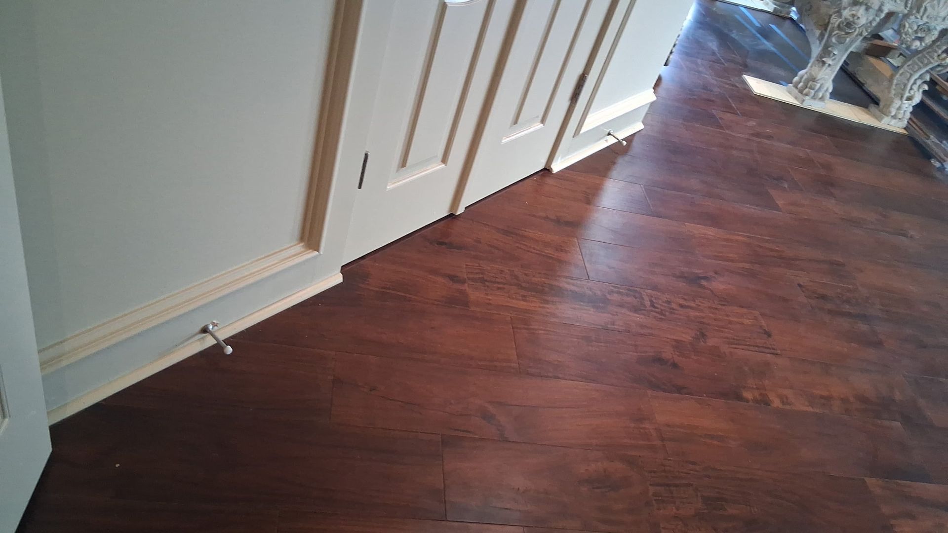 Dark wood floors angled towards a doorway, adjacent to a white wall and door trim.