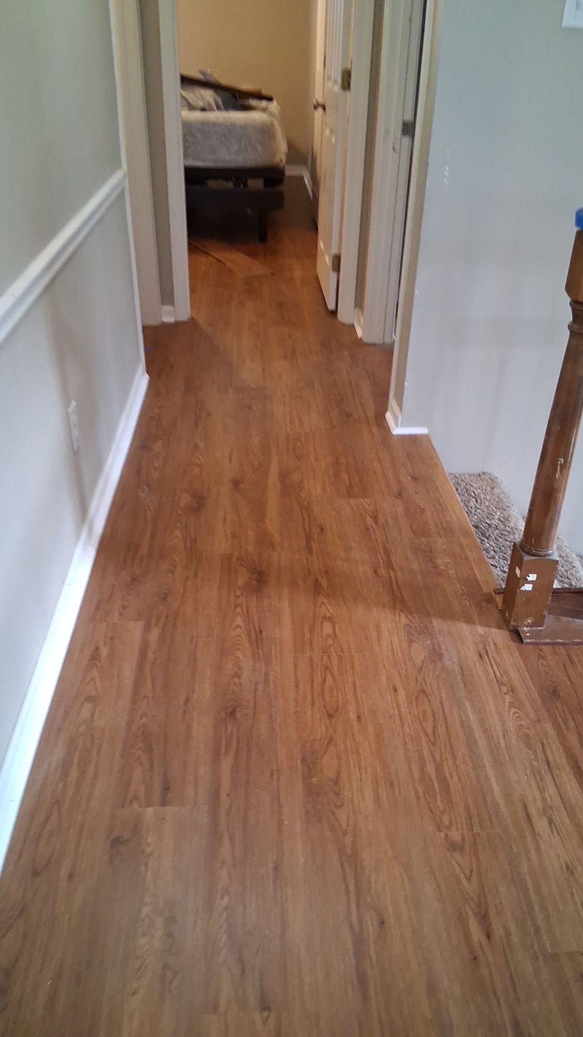 Hallway with wood-look flooring, leading to a bedroom and doorways. White trim and light gray walls.