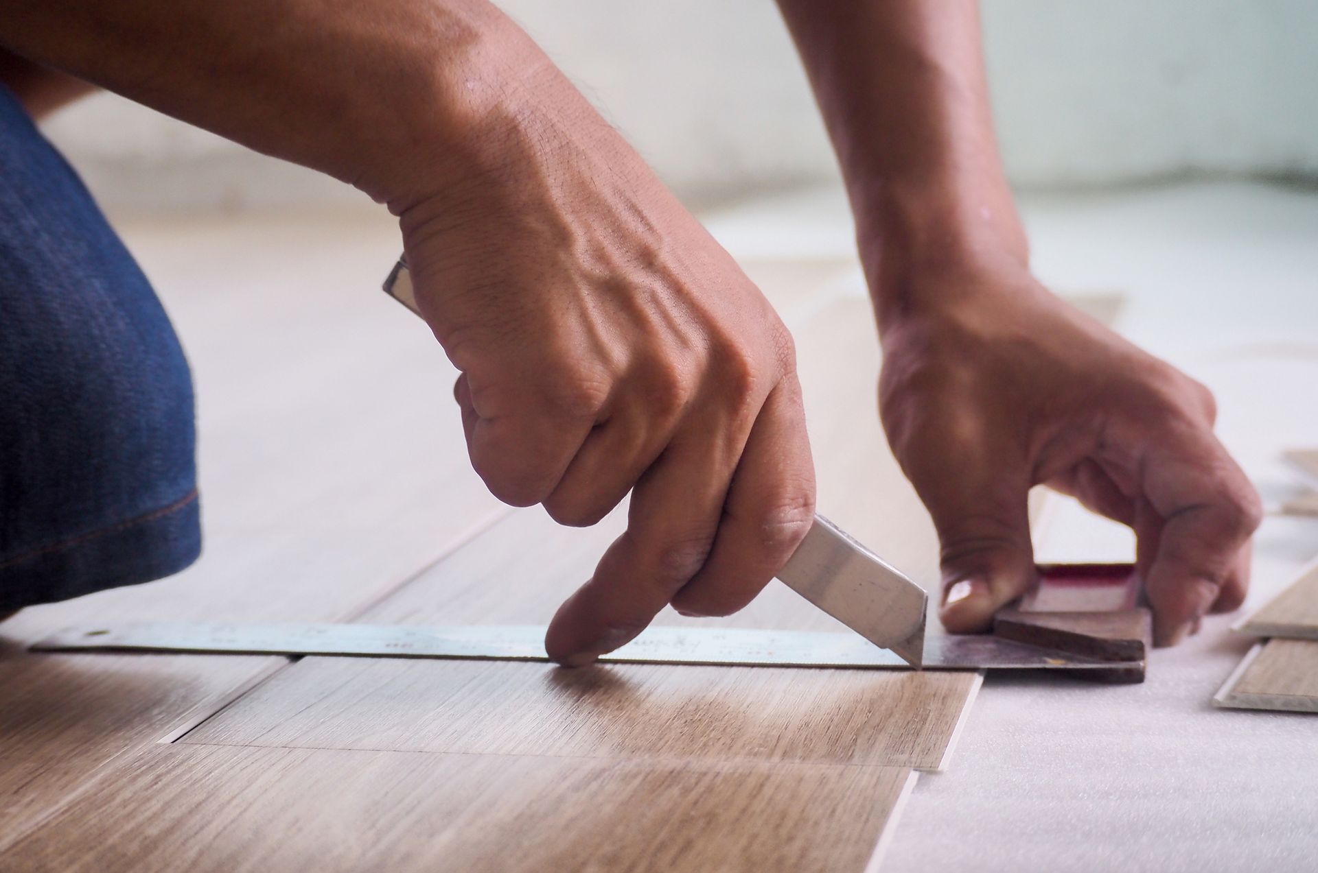 Person using a utility knife to cut flooring tile, kneeling on the floor.