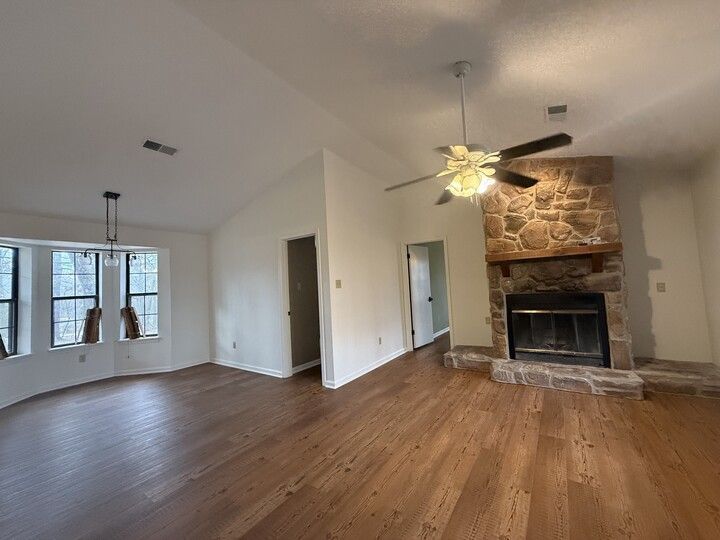 Living room with stone fireplace, wooden floor, and vaulted ceiling.