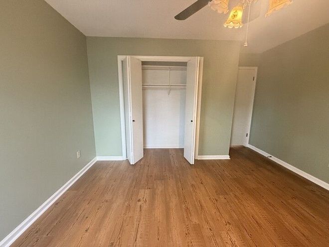 Empty bedroom with light green walls, wood-look floor, and a closet with open white doors.