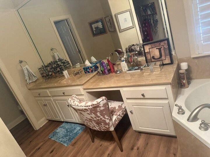 Vanity area in a bathroom with a chair, counter, mirror, and toiletries.
