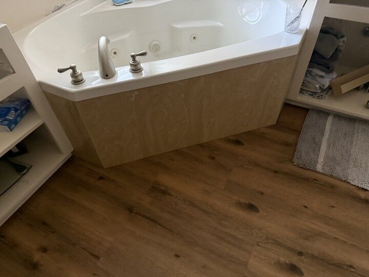 A built-in white bathtub with tan facing, set in a bathroom with wood-look flooring.