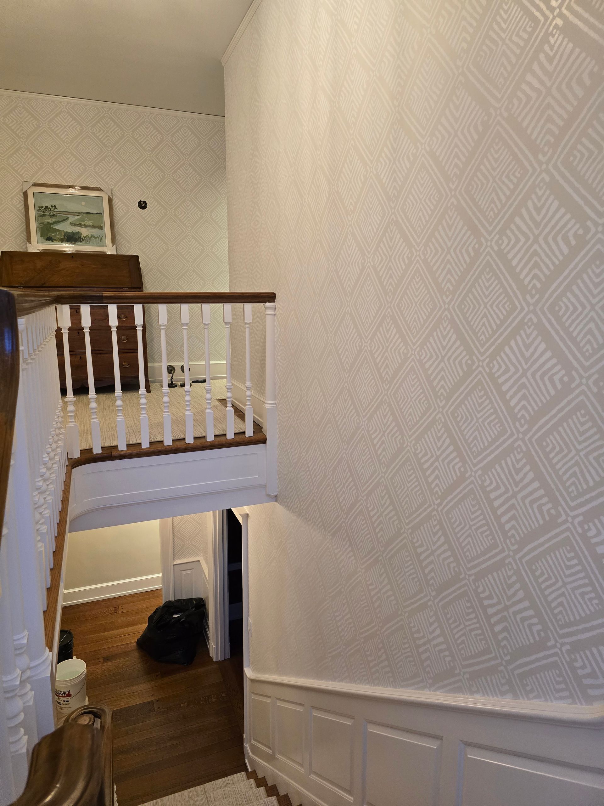 Staircase with white textured wallpaper, wooden steps, and a white railing. Doorway at the bottom with dark objects.