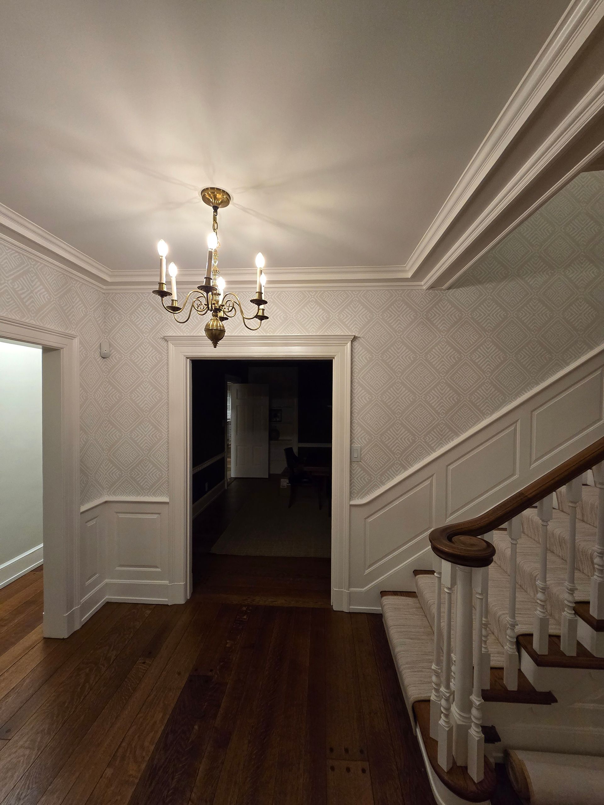 Hallway with chandelier, patterned wallpaper, and staircase.