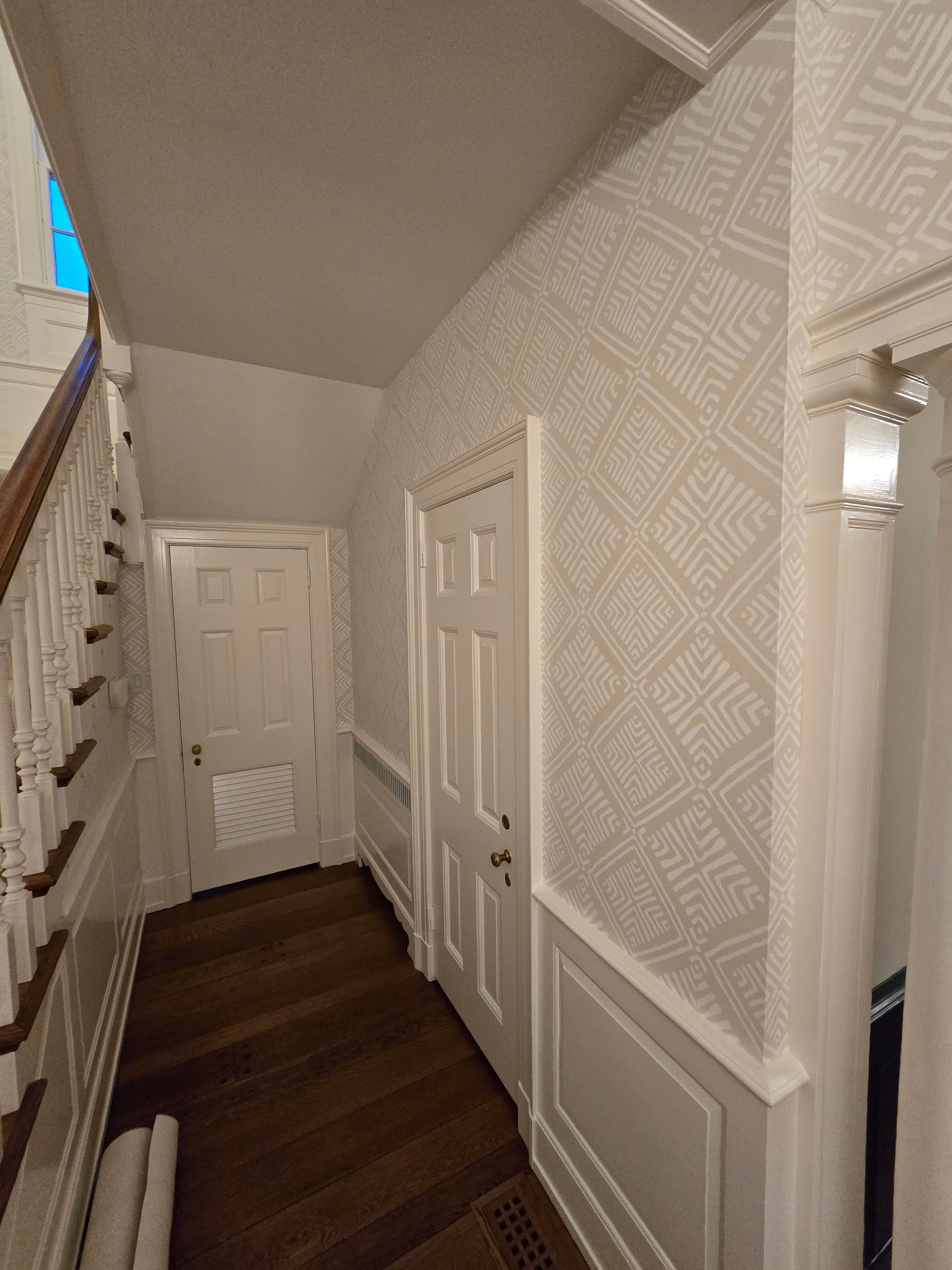 Hallway with wallpaper, white doors and trim, and a dark wood floor. Staircase on the left.
