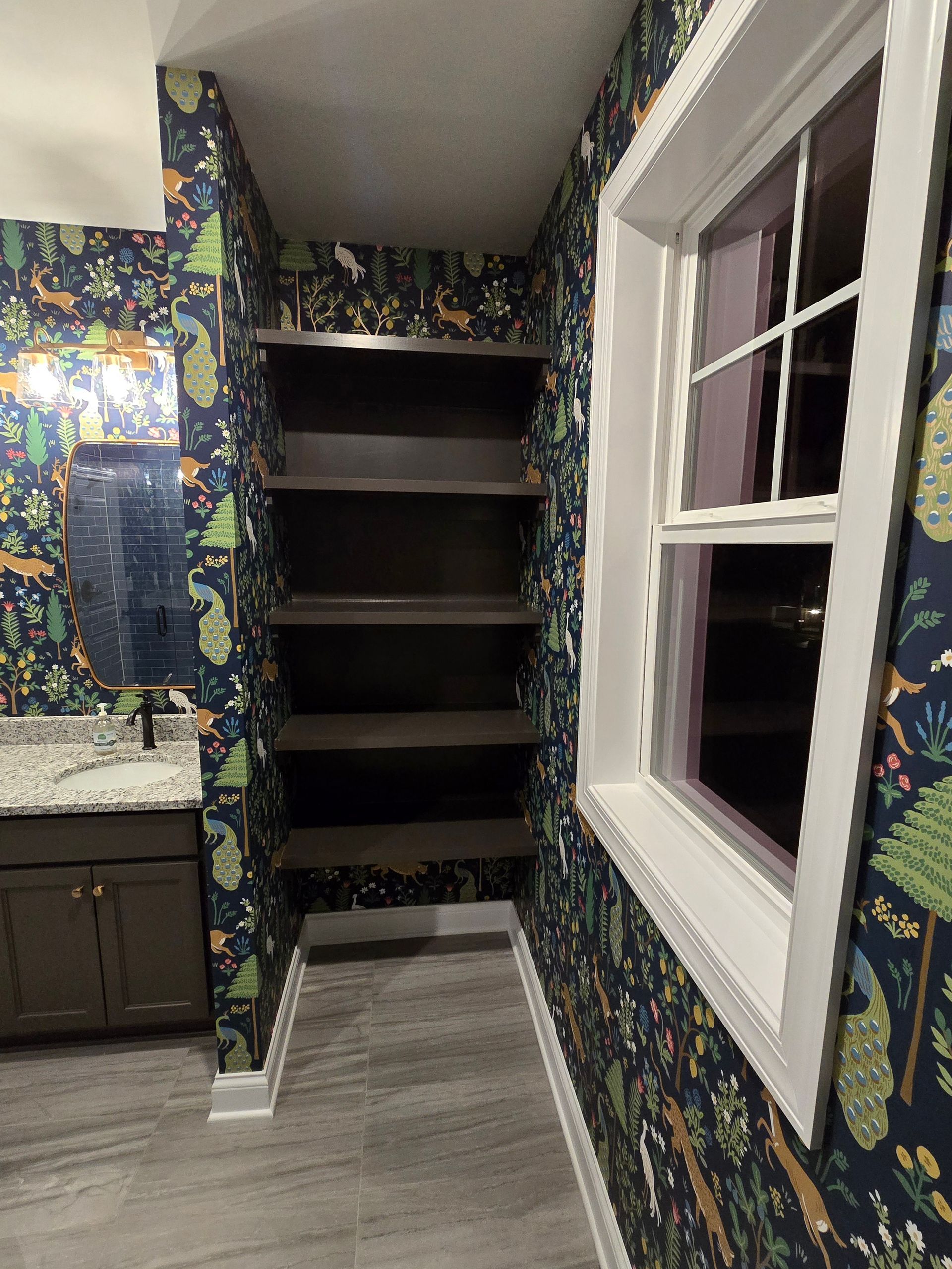 Bathroom with patterned wallpaper, built-in shelves, and a window with white trim.