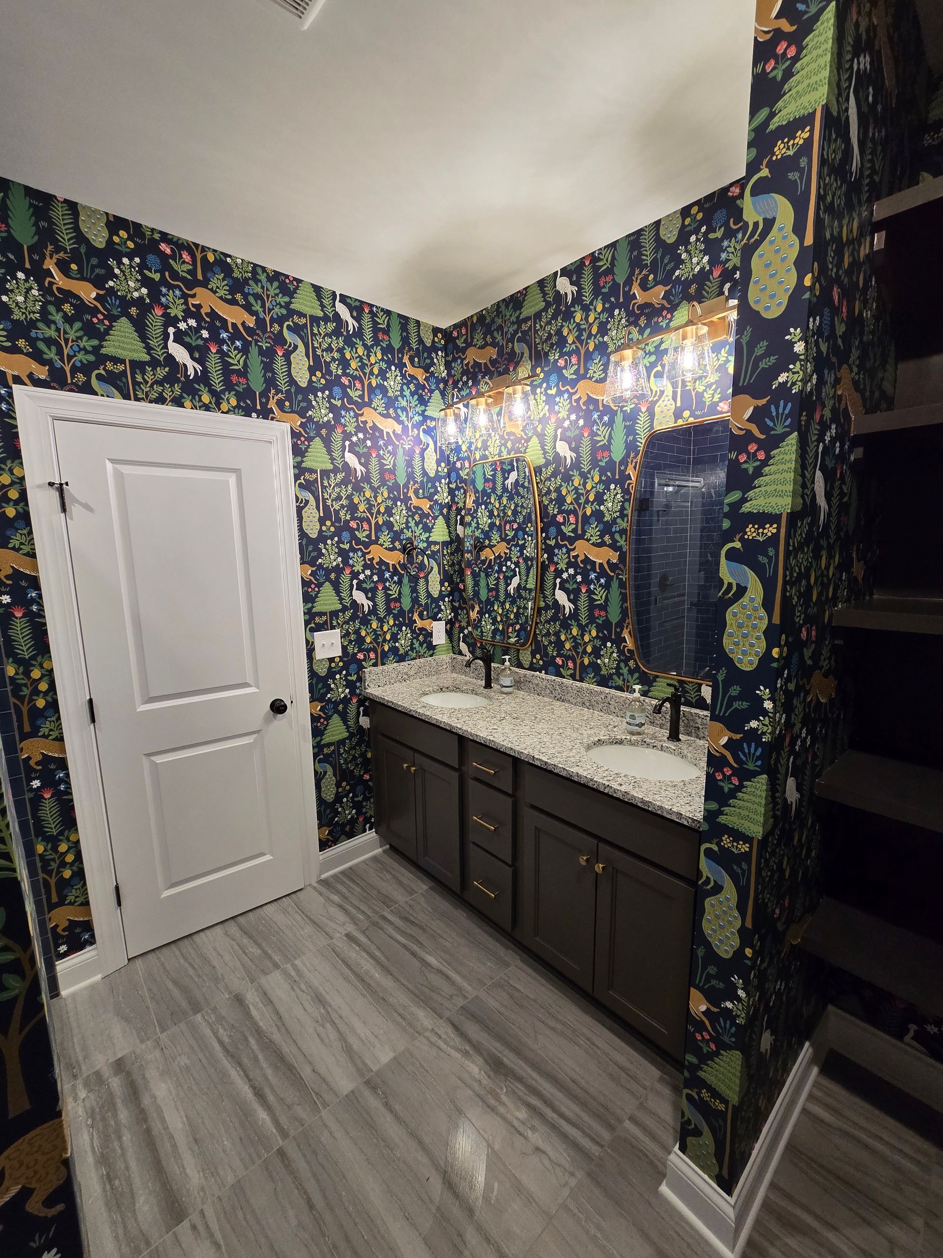 Bathroom with dinosaur wallpaper, gray floor, dark brown vanity, double sinks, and white door.
