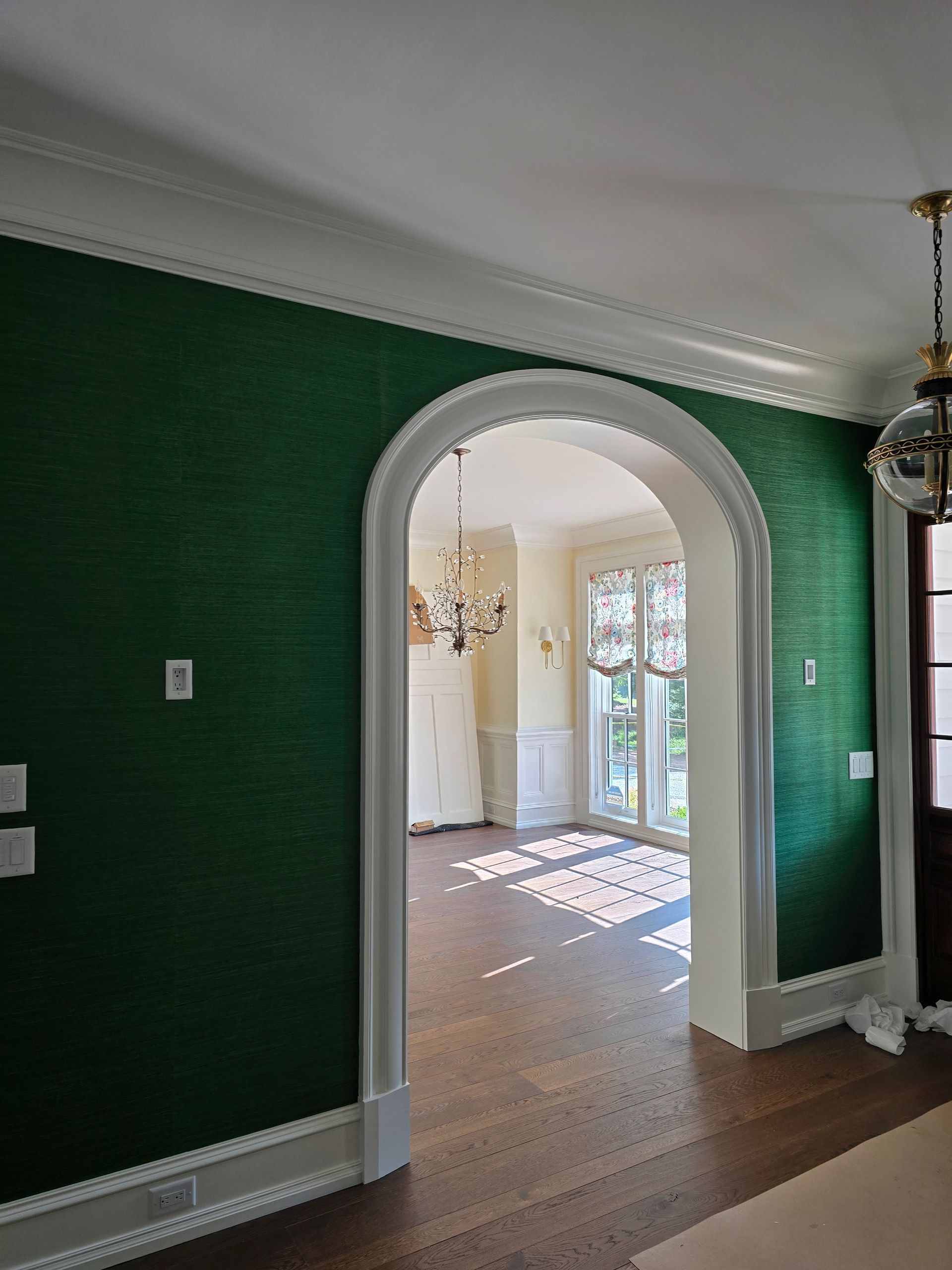 Green textured wall with white trim and arched doorway leading to a sunlit room.