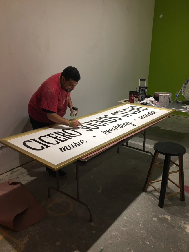 A man is painting a sign that says cigars