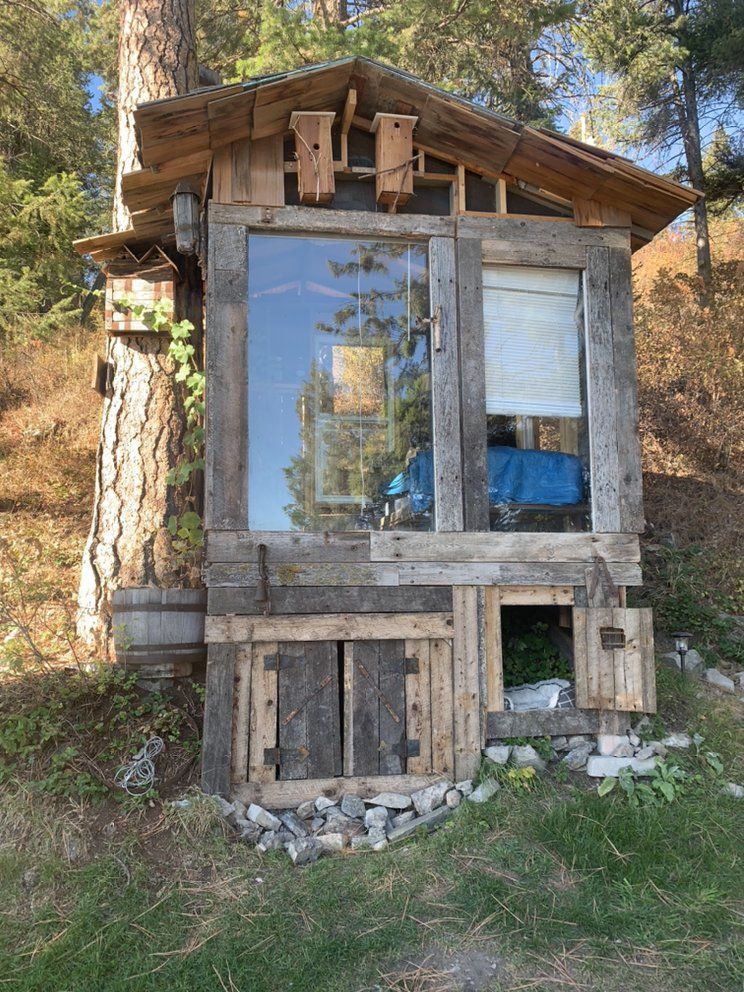 A small wooden house with a large window is sitting on top of a grassy hill.
