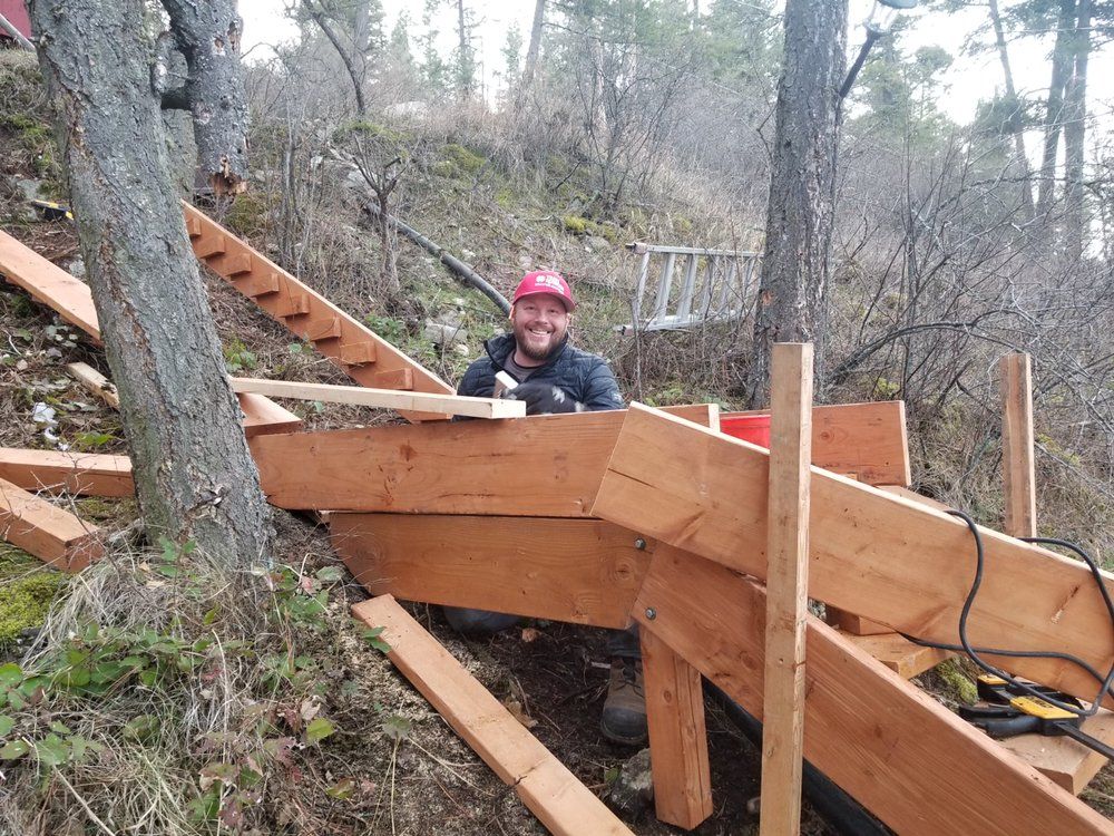 A man is sitting on a wooden staircase in the woods.