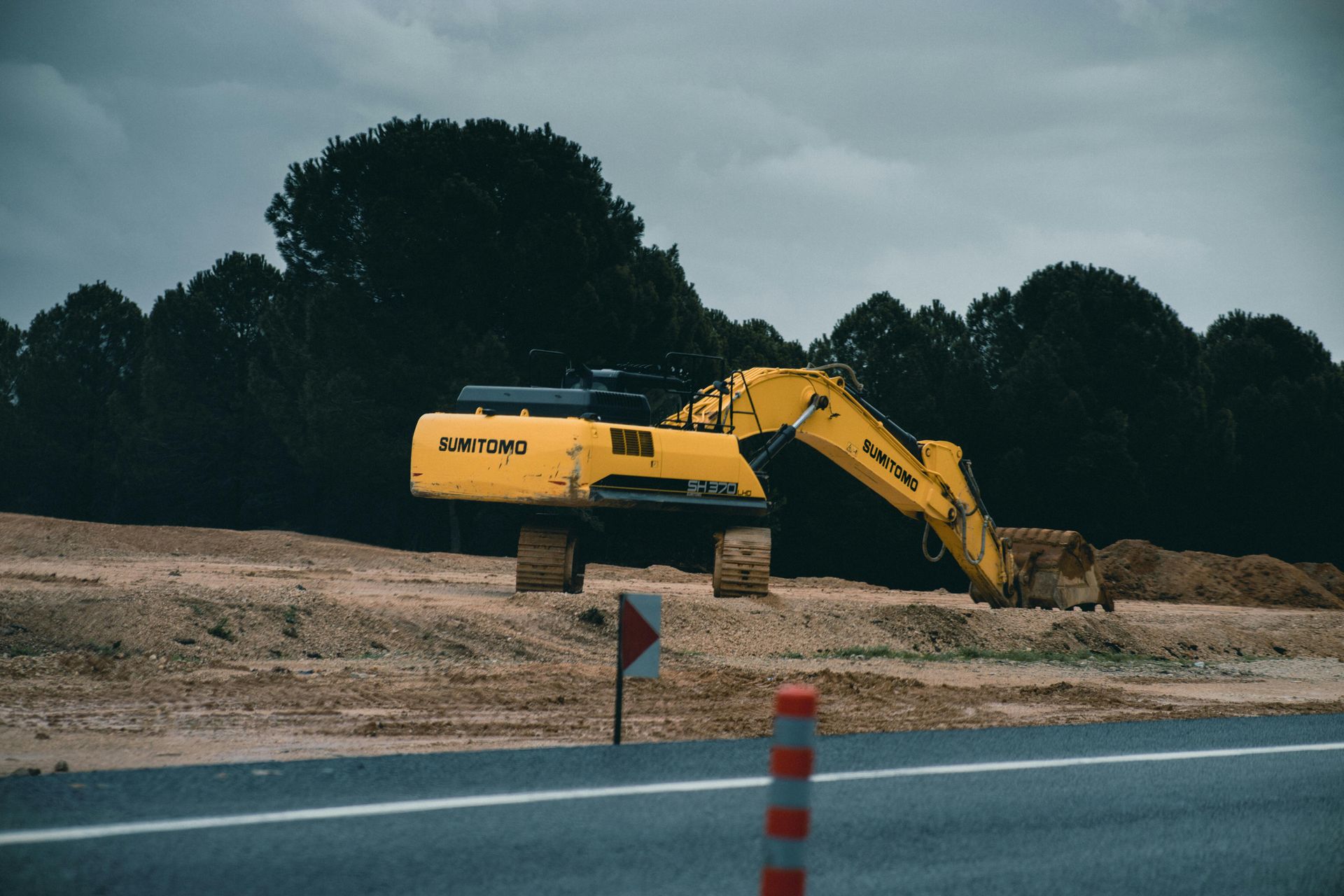 A yellow excavator is sitting on top of a dirt field next to a road.