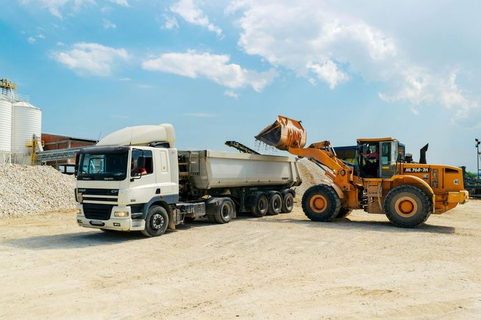 A dump truck is being loaded with sand by a bulldozer.