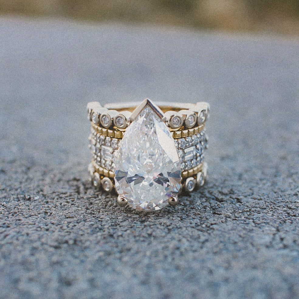 A pear-shaped diamond ring set with multiple bands featuring small diamonds, gold beading, and bezel-set stones.