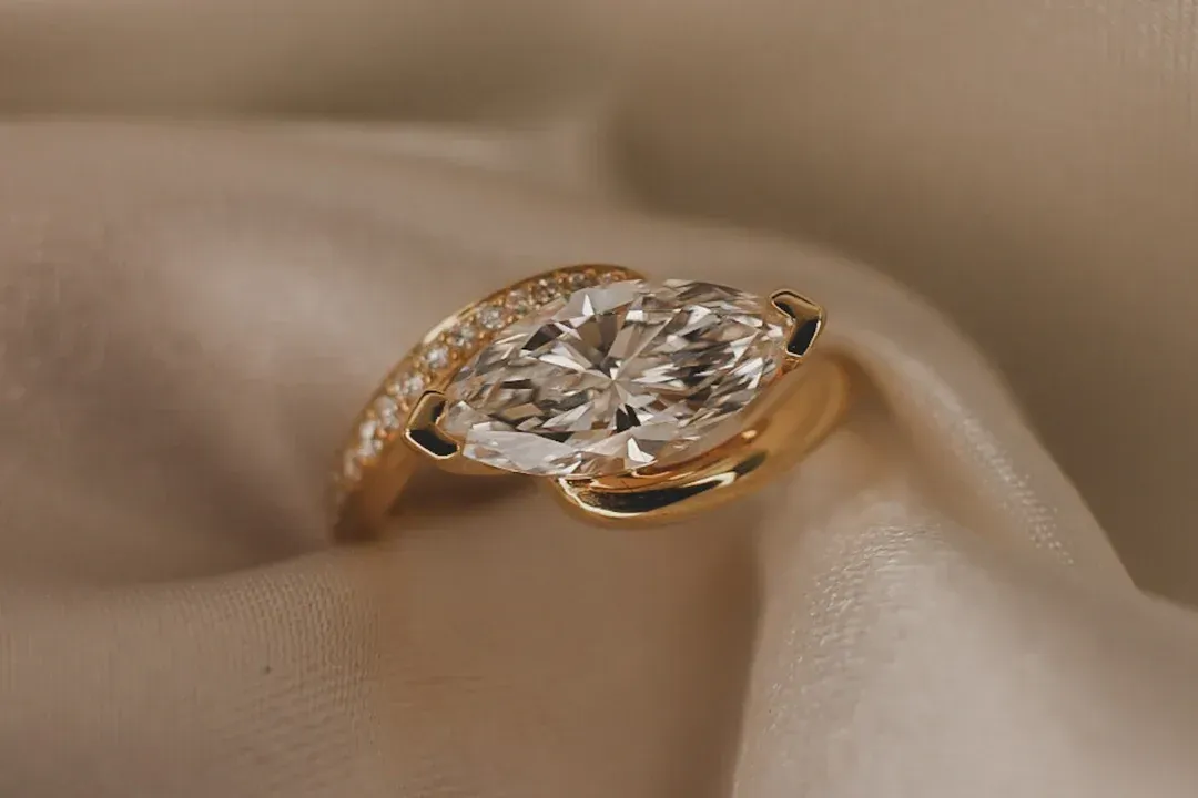 A gold marquise-cut diamond ring resting on soft, beige draped fabric.