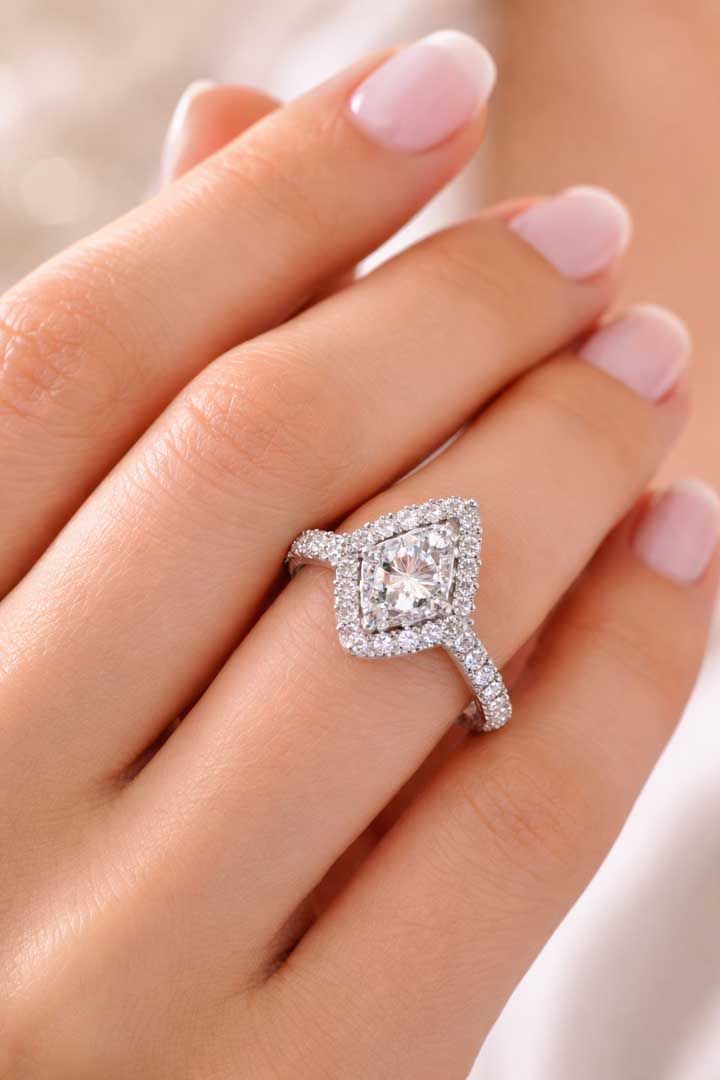 A hand wearing a silver ring featuring a marquise-shaped center stone surrounded by a halo of smaller white diamonds.
