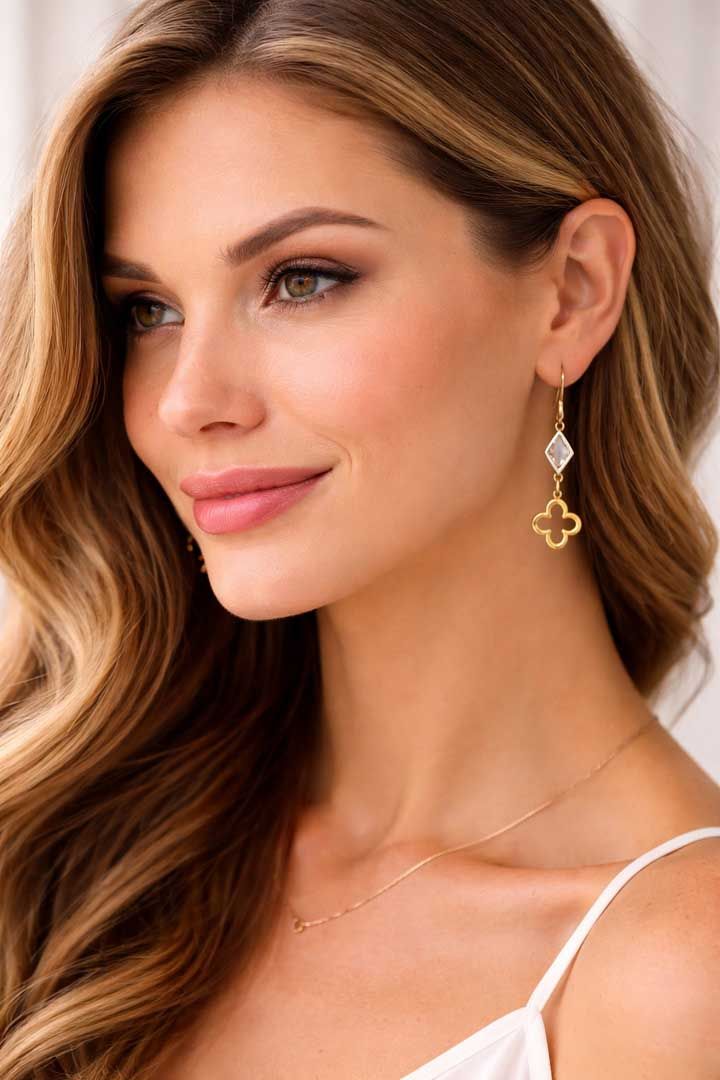 A close-up portrait of a person wearing gold earrings with a small white diamond shape and a gold clover charm.