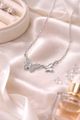 A silver necklace featuring two butterfly charms rests on a silky, light-colored fabric near jewelry and perfume.