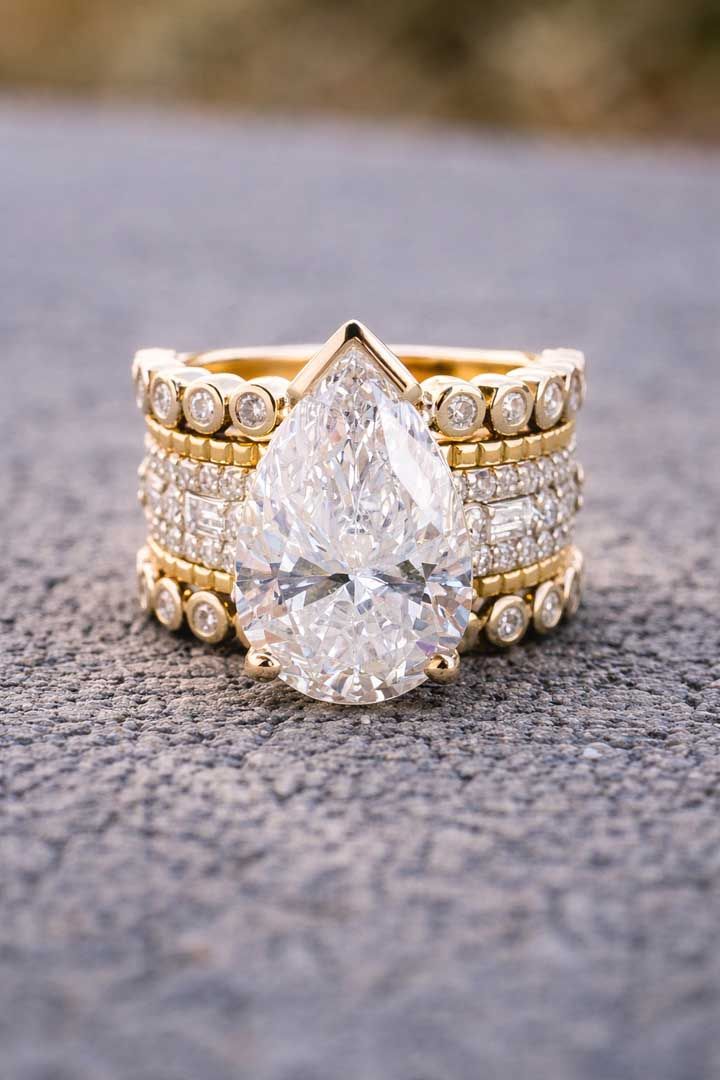 A gold pear-cut diamond ring featuring a thick, layered band set with multiple small diamonds against a grey background.