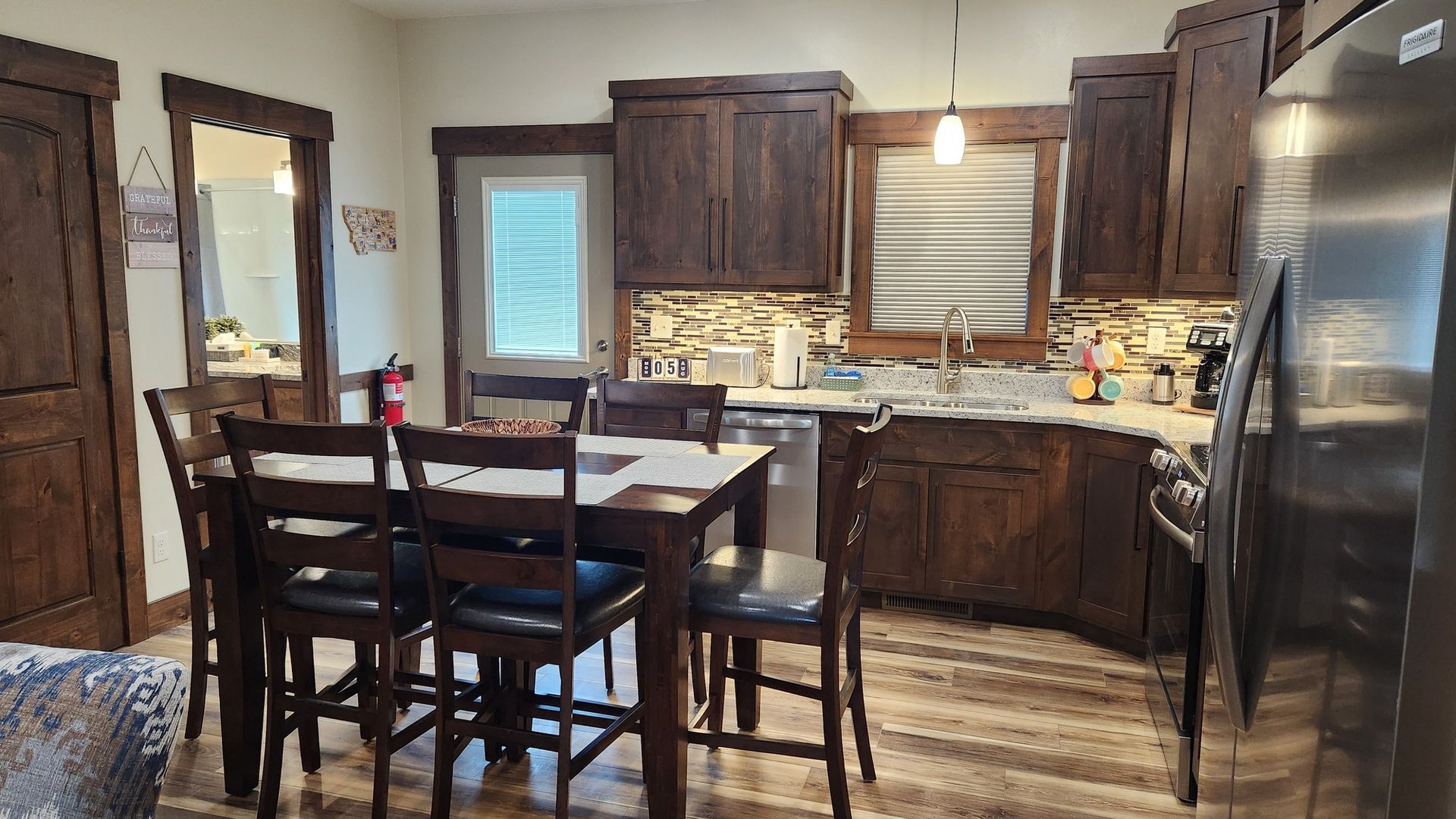 A kitchen with dark wood cabinets, a dining table with six chairs, and a stainless steel refrigerator.