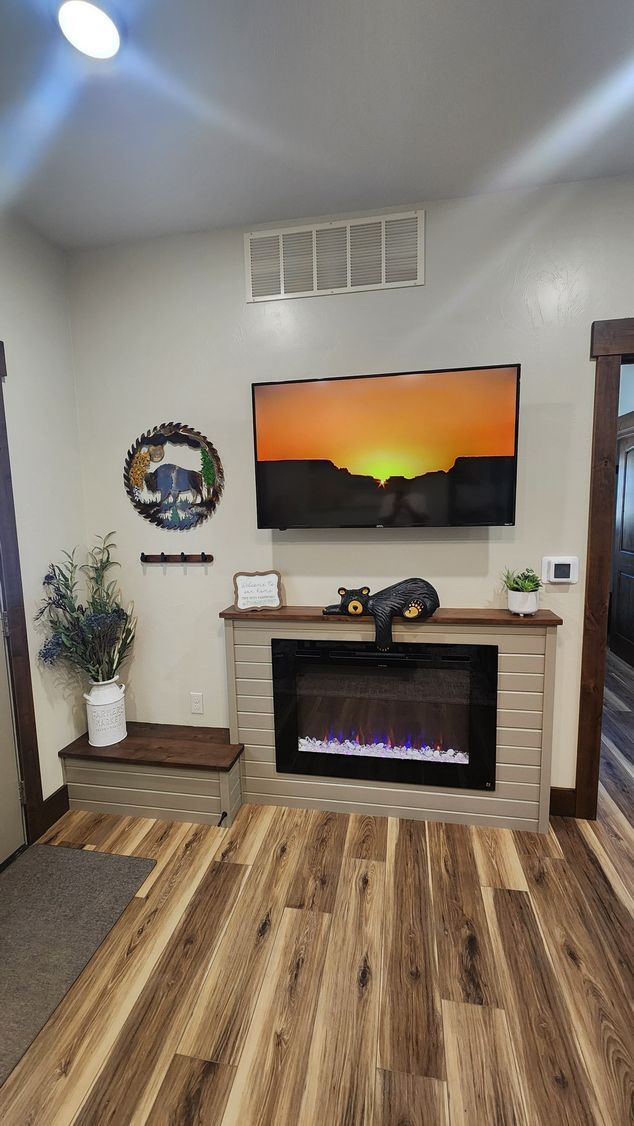 Cozy living room with a fireplace, TV, and wood-look flooring. A decorative cat sits on the mantle.