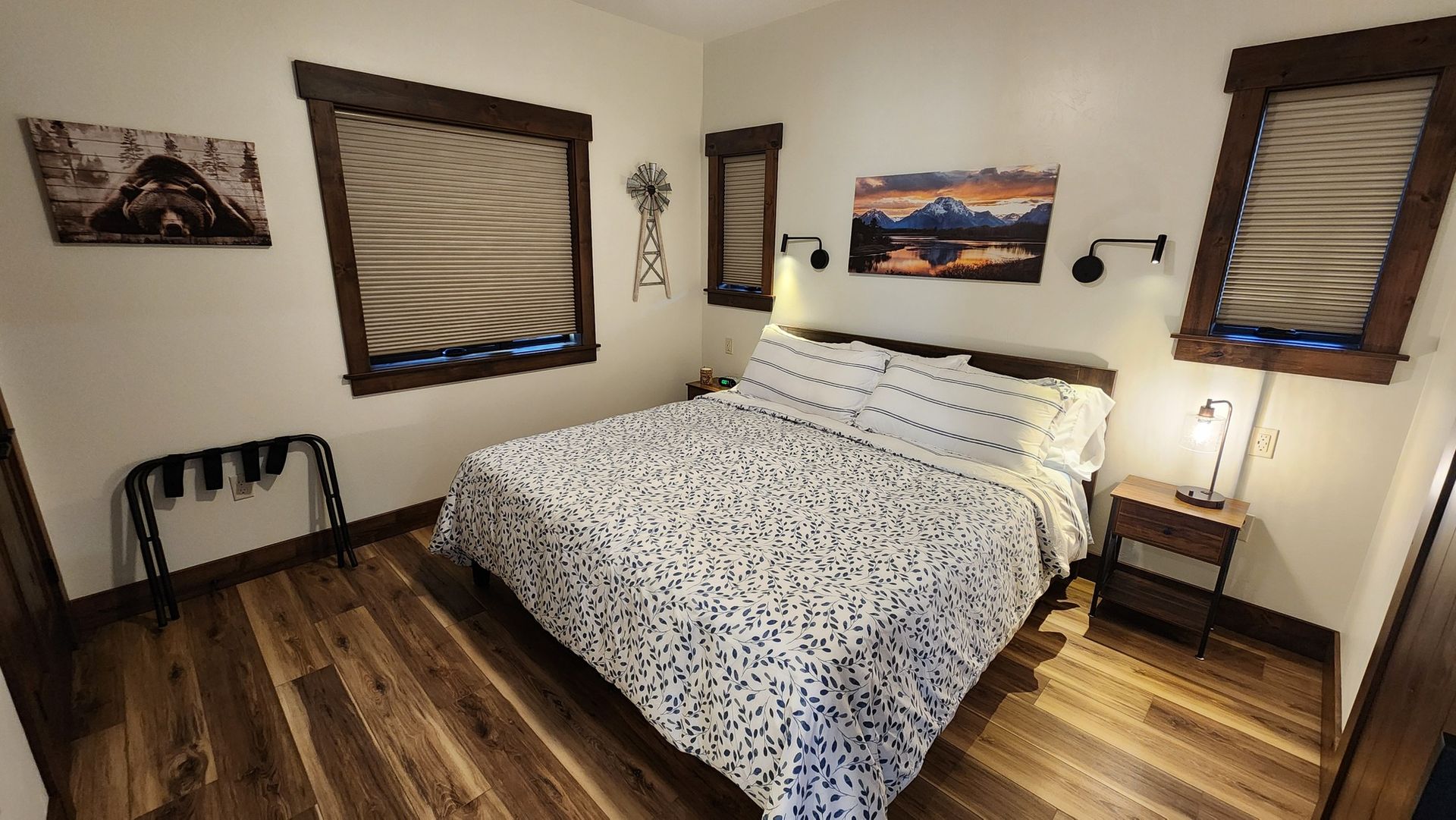 Cozy bedroom with a bed, art, and wood-framed windows. Wooden floors.