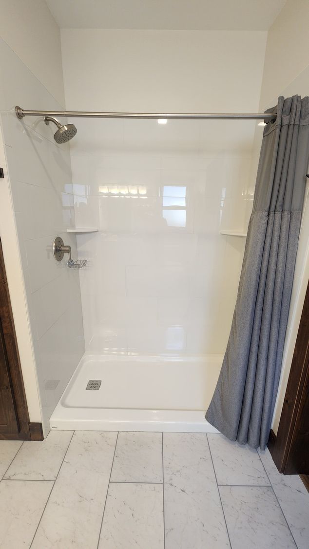 White shower with a gray curtain, chrome fixtures, and a white tiled floor.