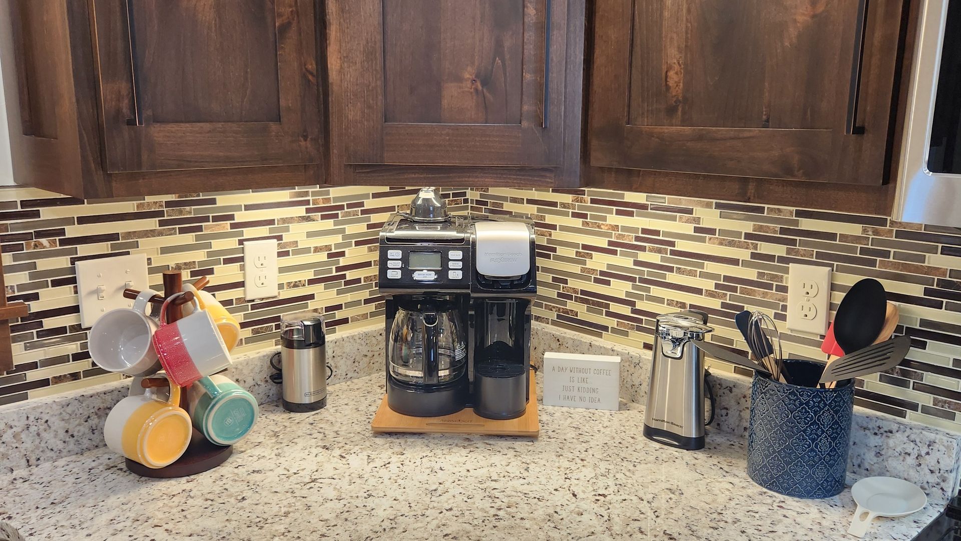 Coffee station with coffee maker, mugs, and utensils on a countertop in a kitchen.