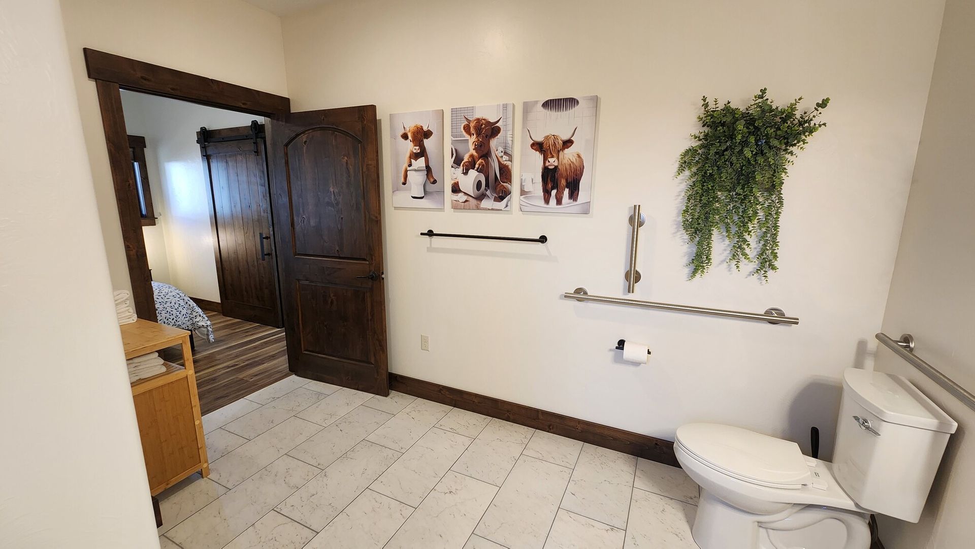 Bathroom with dog art, toilet, grab bars, and hanging plant. Doorway to bedroom.