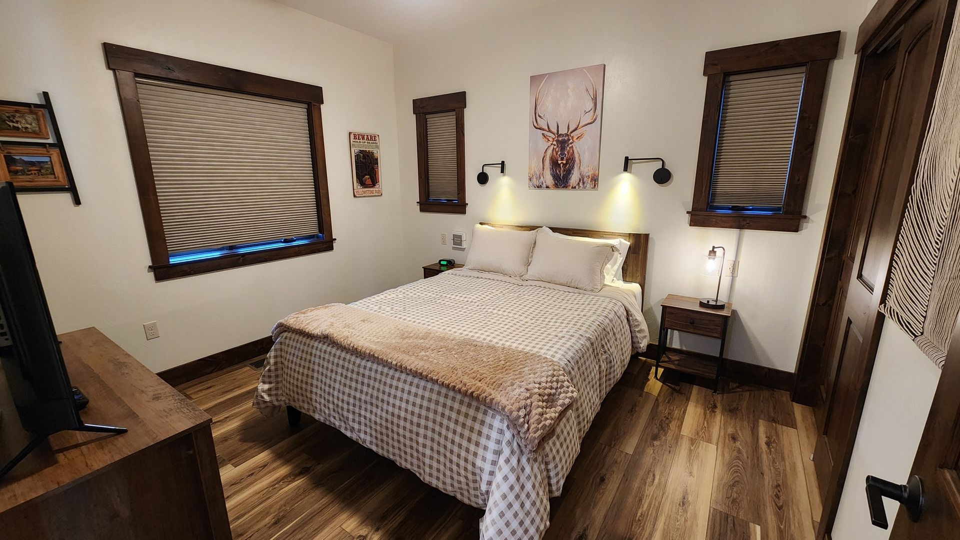 Bedroom with bed, dresser, windows, wooden floors, and deer art.