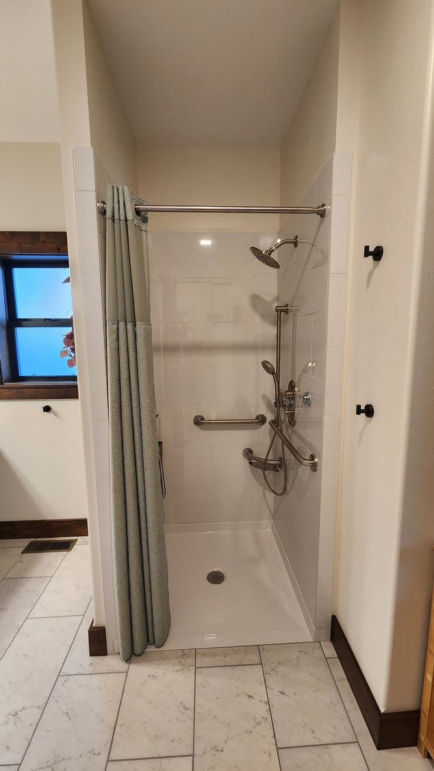Accessible shower with grab bars, shower curtain, and multiple shower heads in a tiled bathroom.