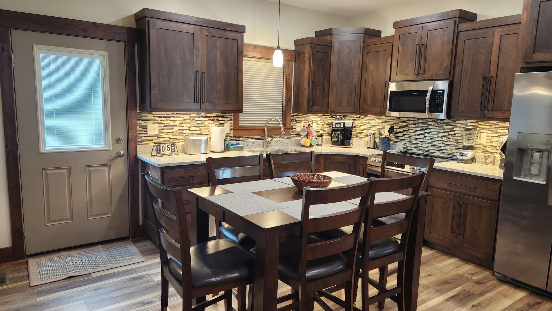 Kitchen with dark wood cabinets, a table with chairs, and a stainless steel microwave and refrigerator.
