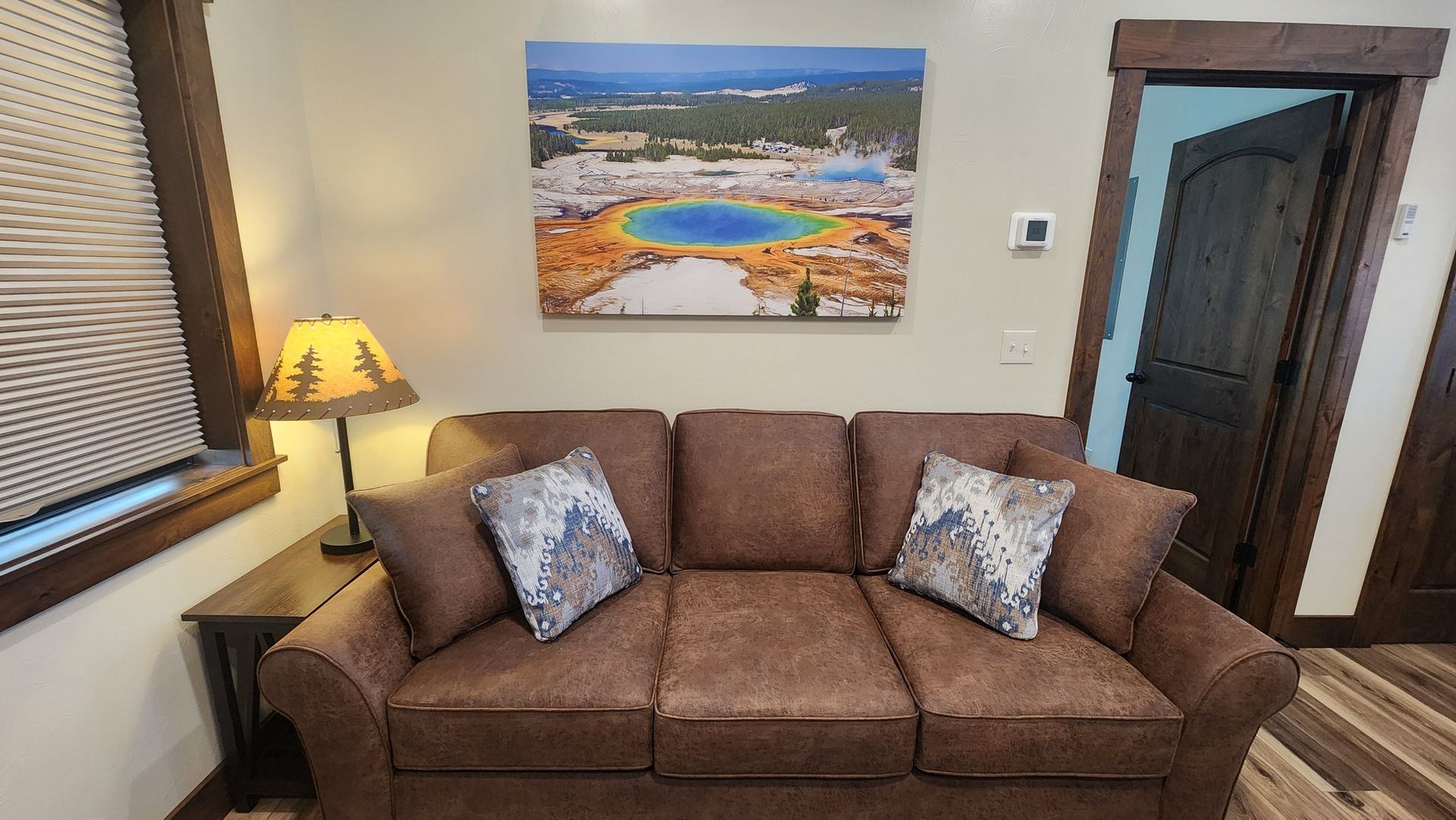 Brown couch in a room with a nature scene painting, lamp, and open door.
