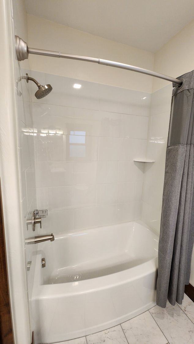 White bathtub and shower with gray shower curtain and fixtures.