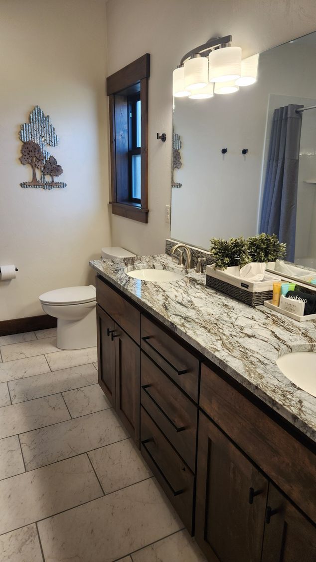 Bathroom with a vanity, toilet, and decorative metal tree on the wall; beige and brown tones.